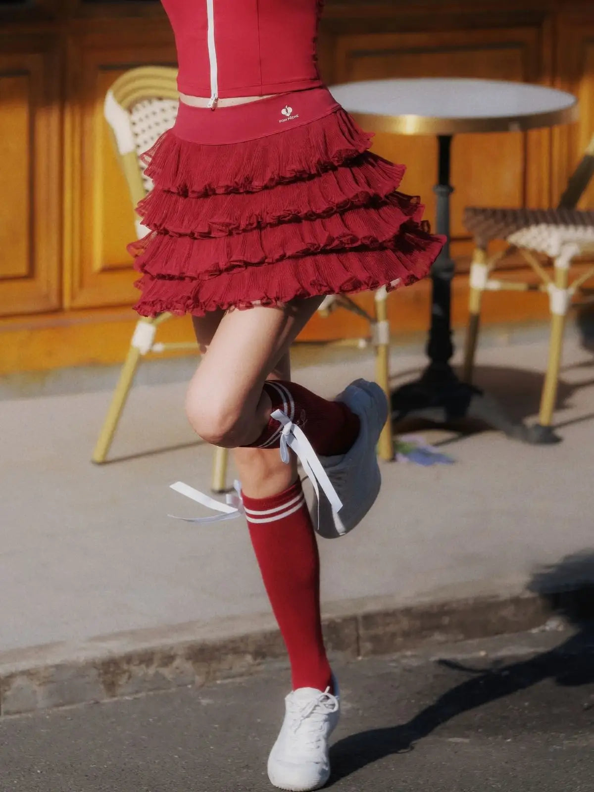 Person wearing a red dress with ruffles, red knee-high socks, and white sneakers on a street.