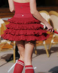 Person wearing a red dress with ruffles and red socks with white stripes, standing outdoors.