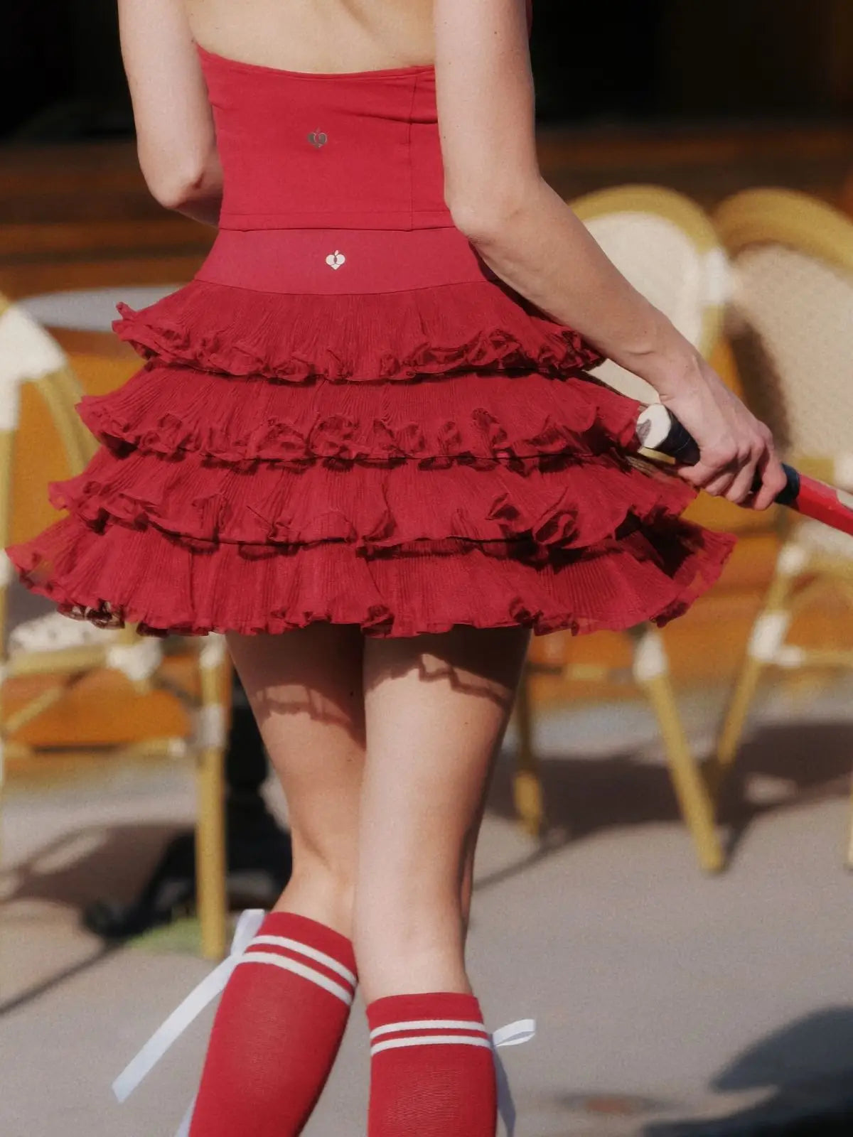 Person wearing a red dress with ruffles and red socks with white stripes, standing outdoors.