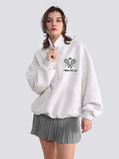 Woman wearing a light gray sweatshirt with a logo and text, standing against a plain background