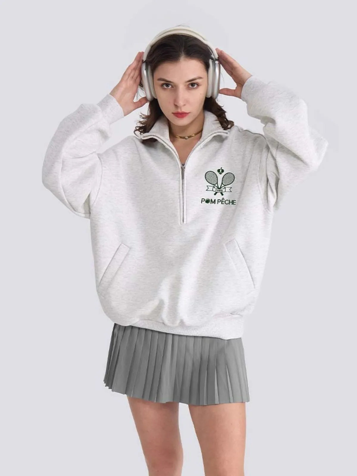 Woman wearing a white sweatshirt with a logo and pleated skirt on a white background