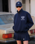 Person wearing a navy blue hoodie and skirt with a logo, standing in front of a vintage car.