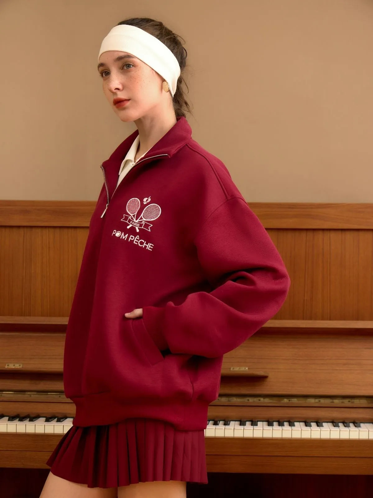 Woman wearing a red sweatshirt with a logo in front of a piano