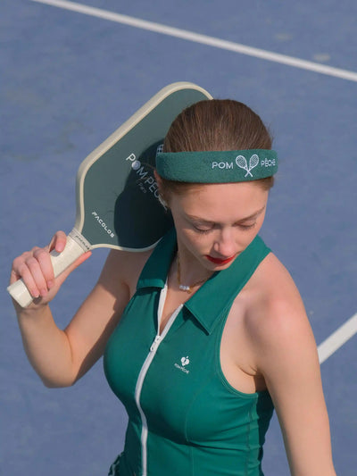 Woman holding a pickleball paddle on a court wearing a green outfit and headband.