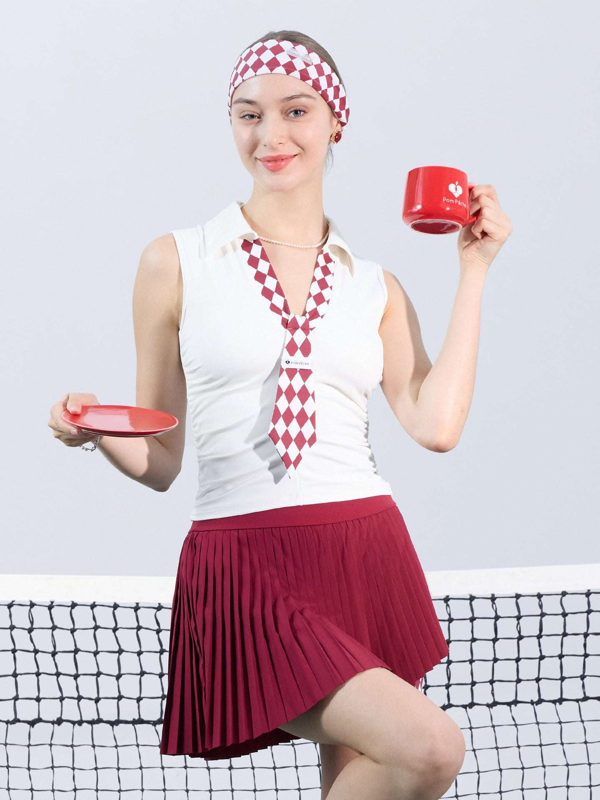 White slim-fit tennis top with a playful red diamond-pattern tie detail, styled for a chic on-court look.