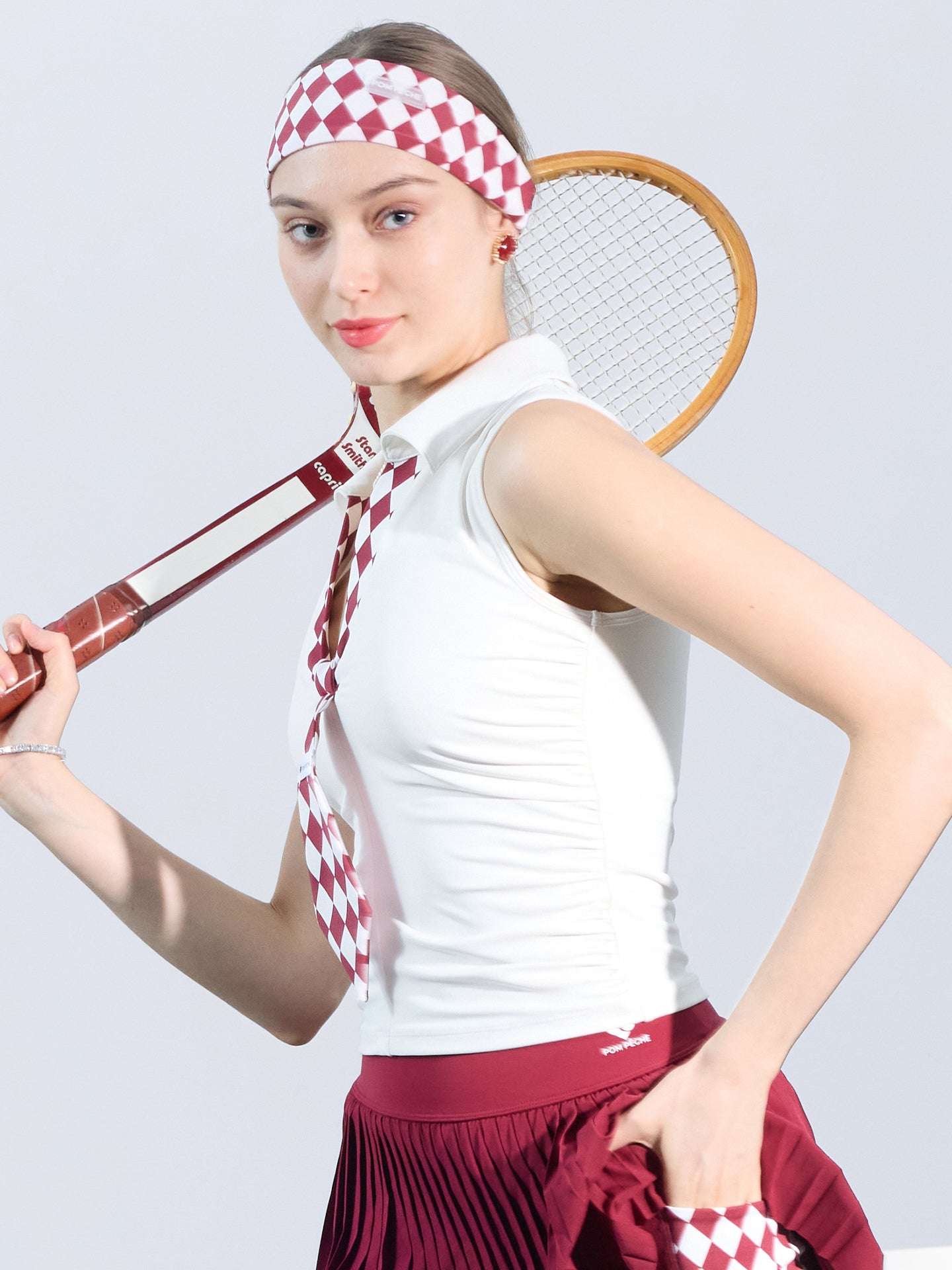 White slim-fit tennis top with a playful red diamond-pattern tie detail, styled for a chic on-court look.