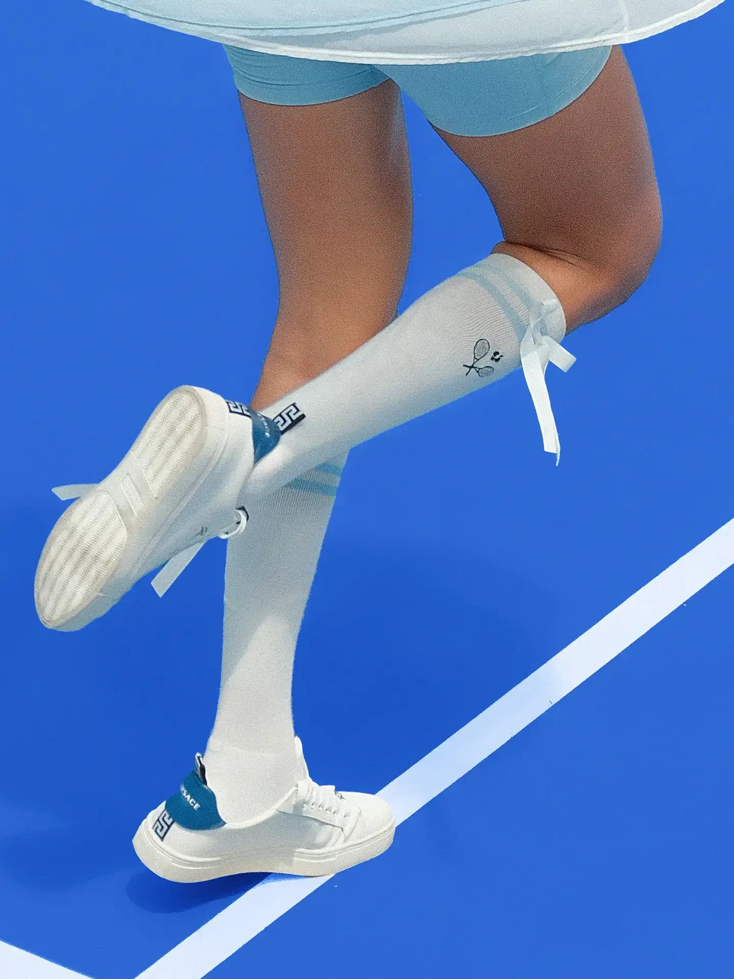 White knee-high tennis socks with sky blue stripes, bow detail, and logo embroidery.