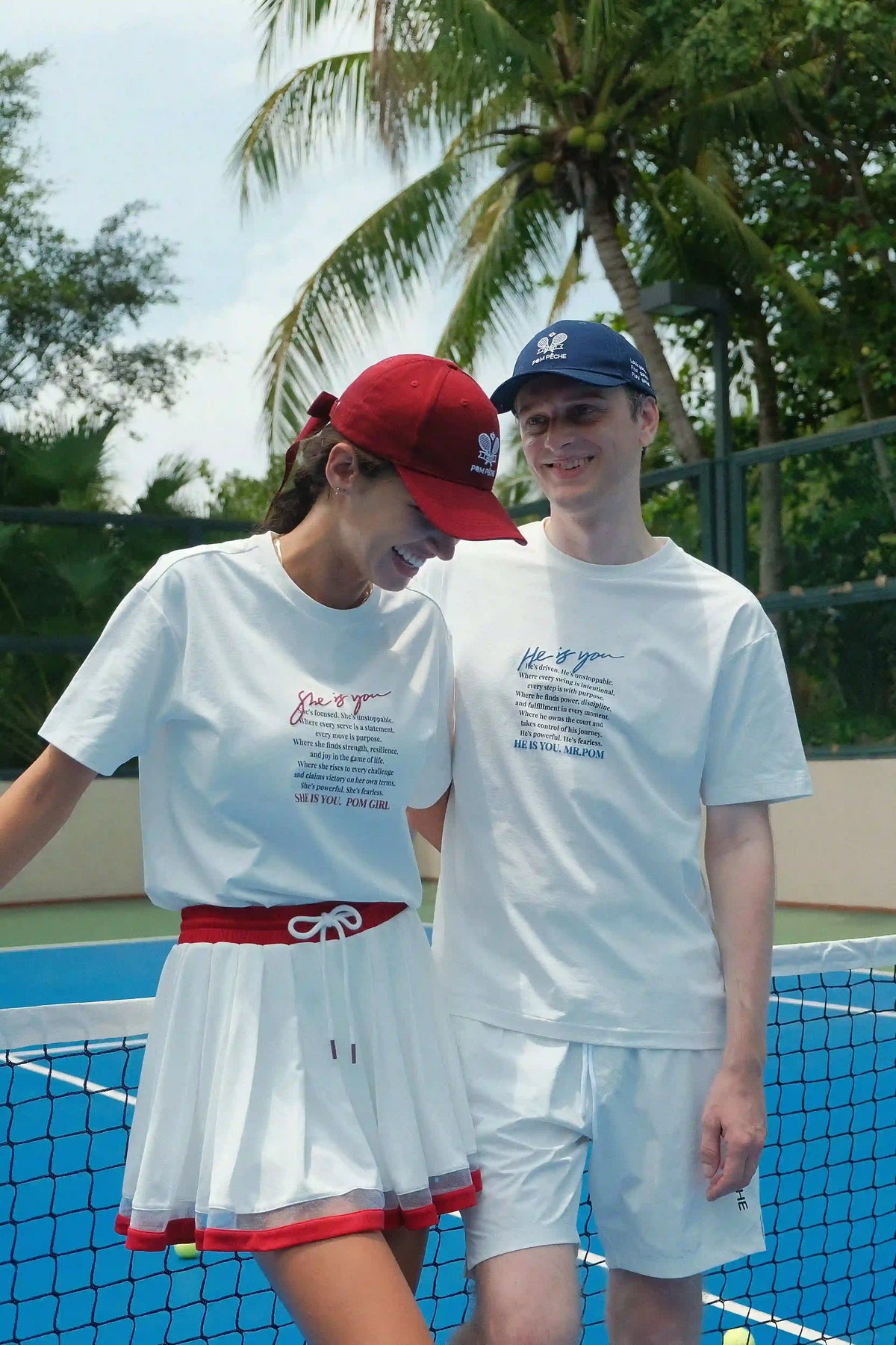 Two people standing on a tennis court with palm trees in the background