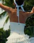 White halter neck crop top with bow detail and subtle logo, styled on the tennis court.