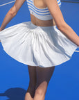 The model is spinning on the court as the white pleated tennis skirt flows with dynamic movement.