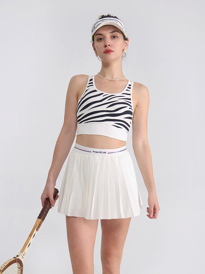 The model is showcasing a white pleated tennis skirt in a clean athletic stance on the court.