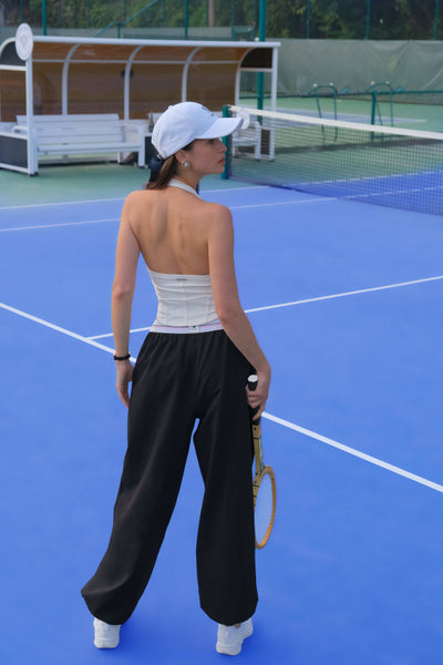 Classical white halter tennis top with a fitted silhouette and subtle logo detail, styled on the tennis court.