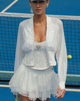 Woman in a white tennis outfit standing on a blue tennis court.