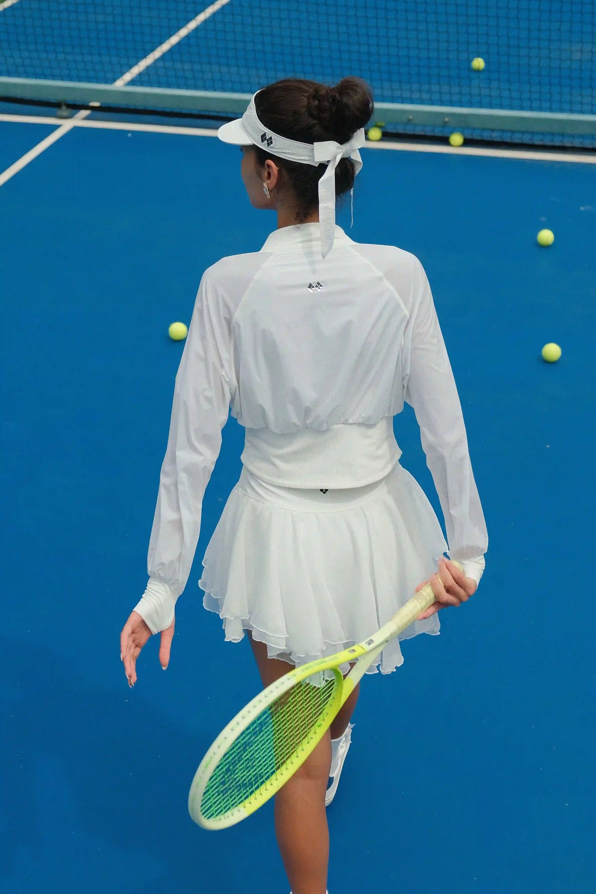 Tennis player in white outfit on a blue court with tennis balls around