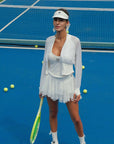 Woman in white tennis attire on a blue tennis court with tennis balls scattered around.