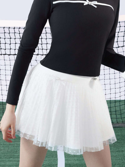 White pleated tennis skirt with soft mesh lace and subtle heart details, offering a lightweight feel, styled on a tennis court. 