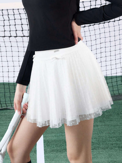 White pleated tennis skirt with soft mesh lace and subtle heart details, offering a lightweight feel, styled on a tennis court. 