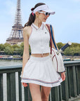 White pleated tennis skirt with red and blue stripes, styled with crop top and visor on a scenic bridge backdrop