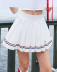 Tennis outfit featuring white pleated skirt and striped hem, posed in an urban riverside walking scene