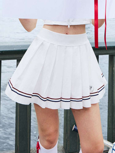 Tennis outfit featuring white pleated skirt and striped hem, posed in an urban riverside walking scene