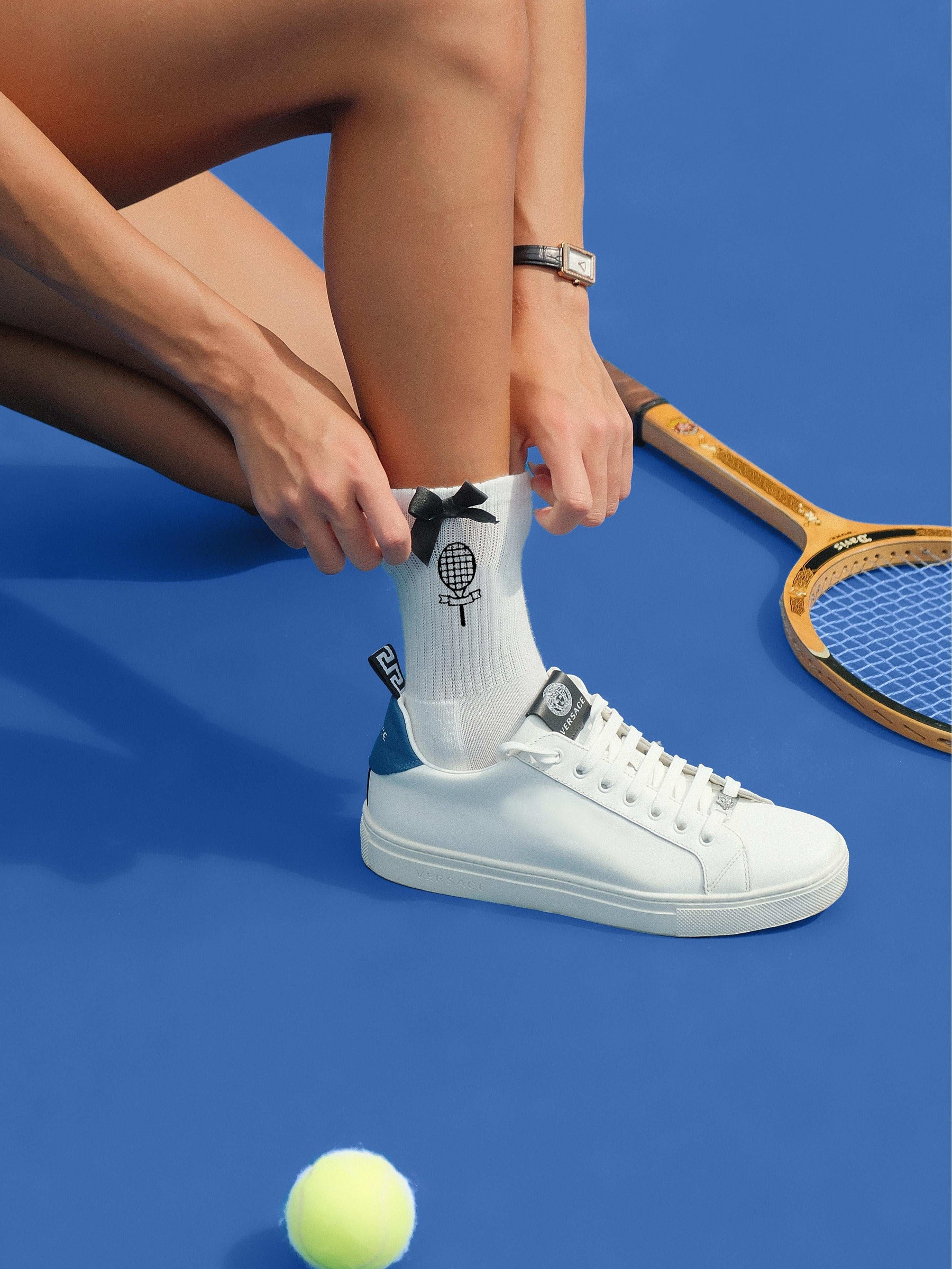 White ankle tennis socks with black bow detail and Pom Pêche logo, styled on the court.