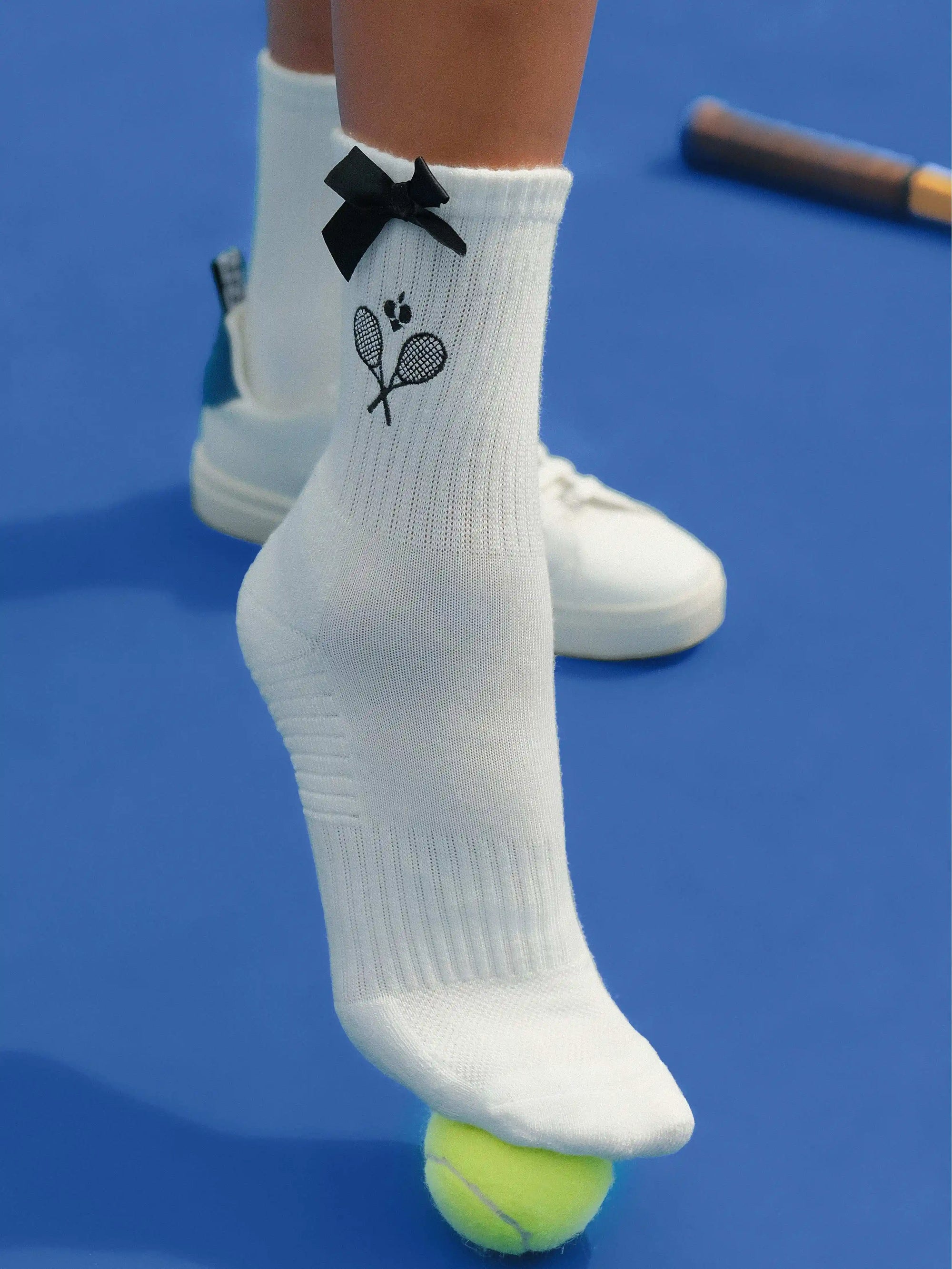 White ankle tennis socks with black bow detail and Pom Pêche logo, styled on the court.