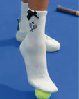 White ankle tennis socks with black bow detail and Pom Pêche logo, styled on the court.