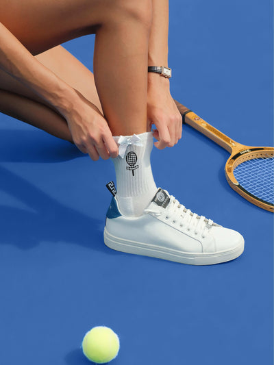 White ankle tennis socks with black bow detail and Pom Pêche logo, styled on the court.
