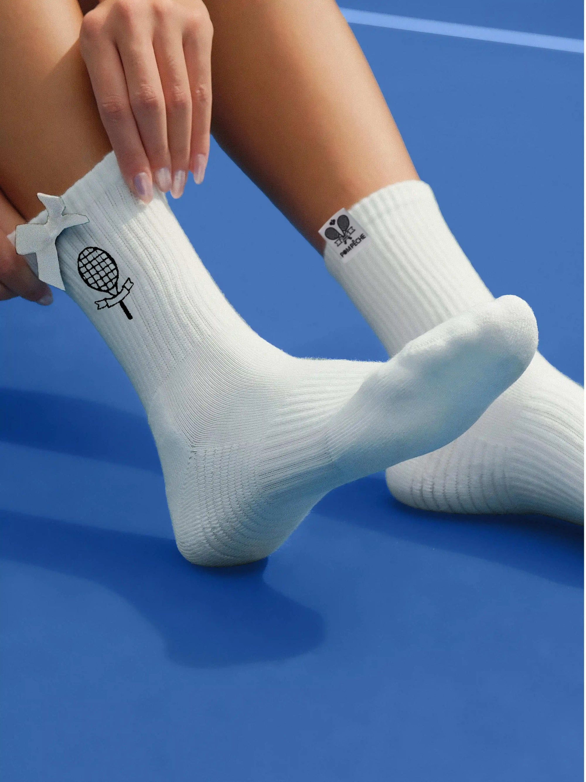 White ankle tennis socks with black bow detail and Pom Pêche logo, styled on the court.