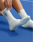 White ankle tennis socks with black bow detail and Pom Pêche logo, styled on the court.