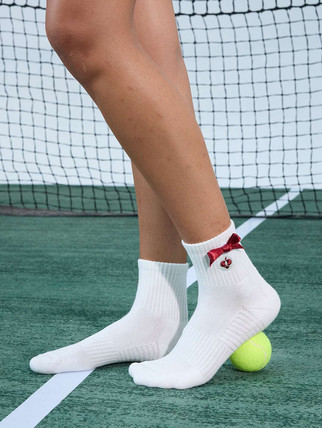 White ankle tennis socks with red bow detail and Pom Pêche logo, styled on the court