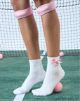 White ankle tennis socks with red bow detail and Pom Pêche logo, styled on the court.