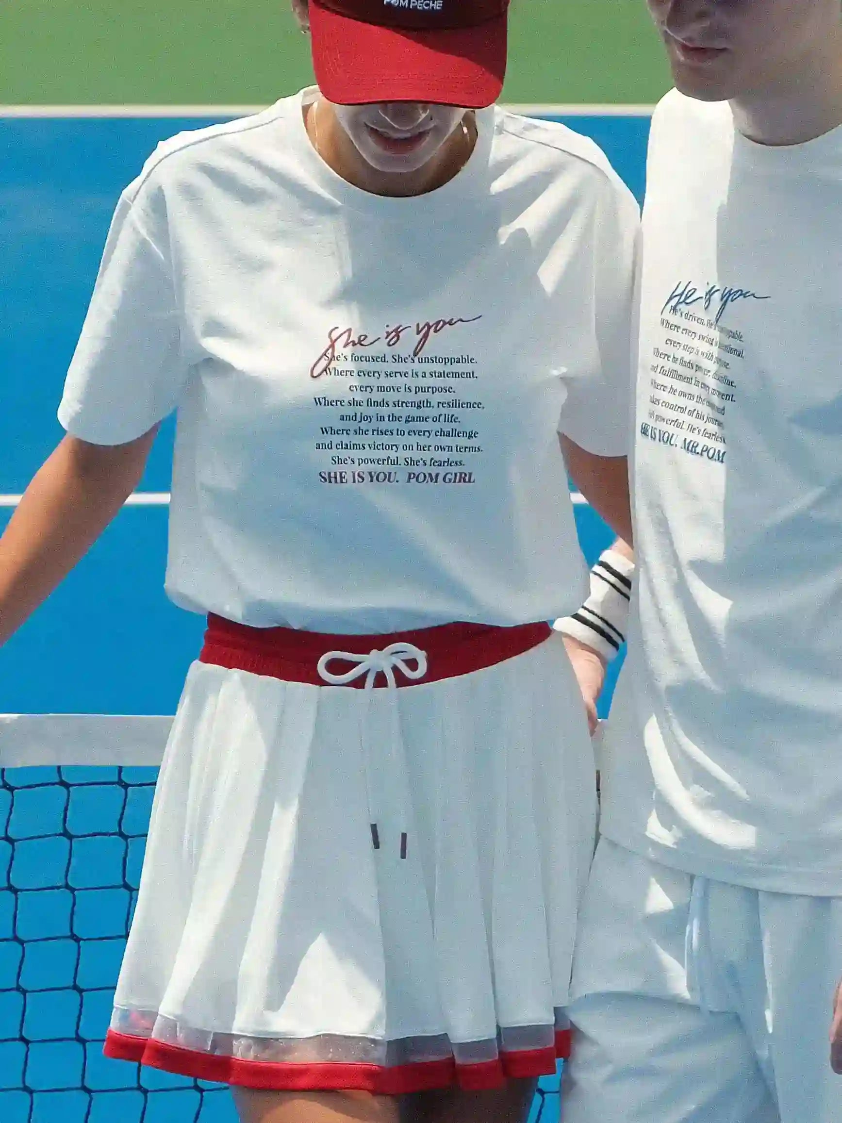 Two people wearing white t-shirts with text on a tennis court.