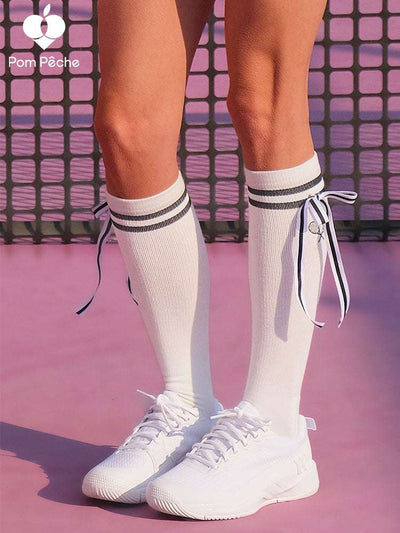 White knee-high tennis socks with black stripes, bow detail, and logo embroidery.
