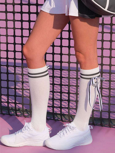 White knee-high tennis socks with black stripes, bow detail, and logo embroidery.