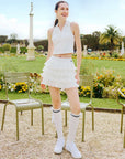 White cropped tennis top with ruffled collar and sleeveless design, featuring a subtle logo for a chic, sporty look.