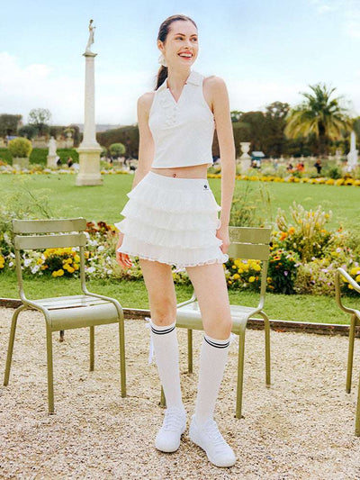 White cropped tennis top with ruffled collar and sleeveless design, featuring a subtle logo for a chic, sporty look.