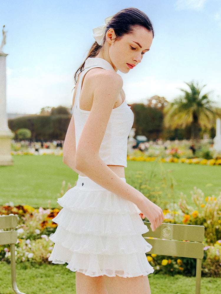 White cropped tennis top with ruffled collar and sleeveless design, featuring a subtle logo for a chic, sporty look.
