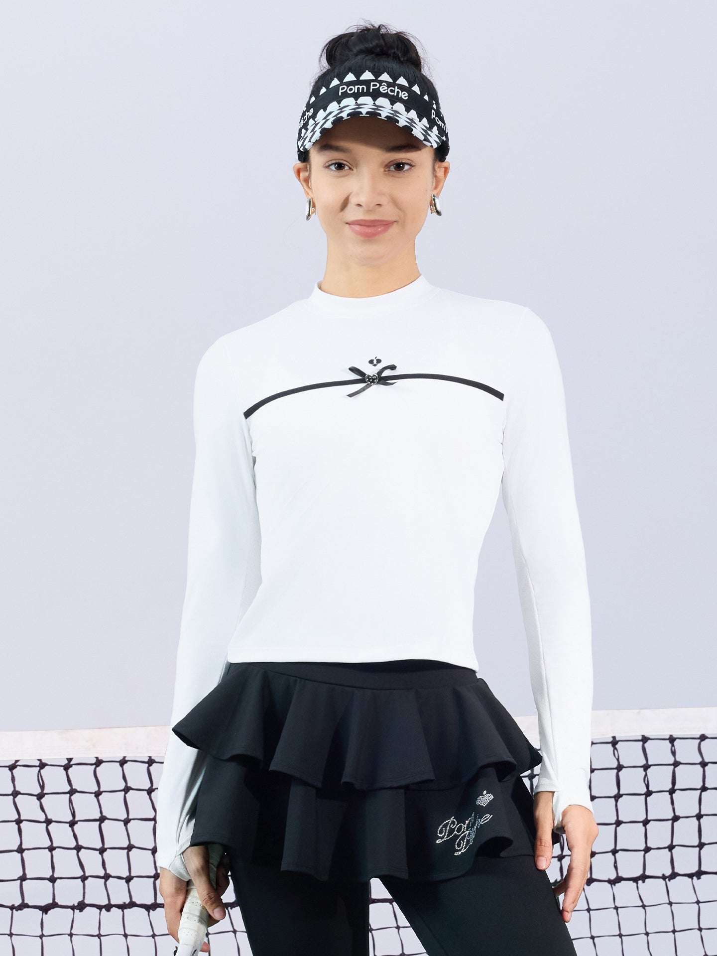 White long-sleeve top with a smooth silhouette and contrast bow detail, styled on the tennis court.