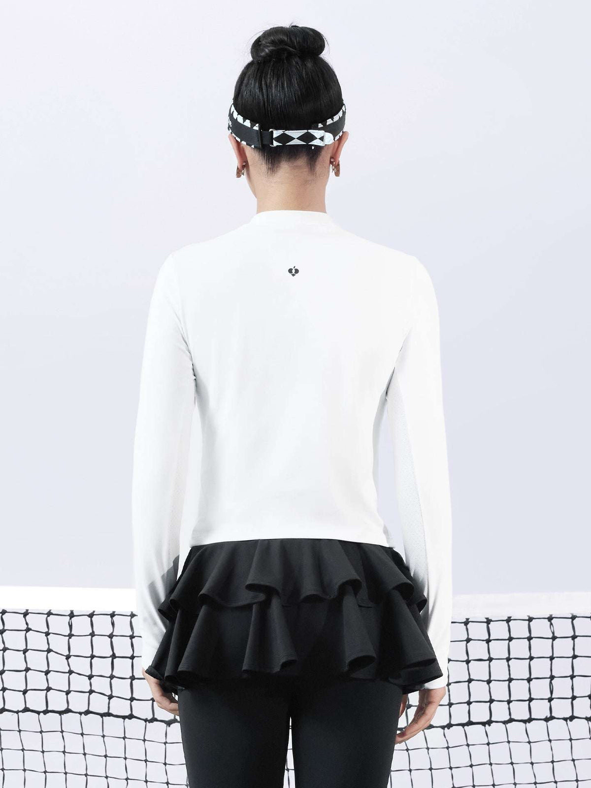 White long-sleeve top with a smooth silhouette and contrast bow detail, styled on the tennis court.