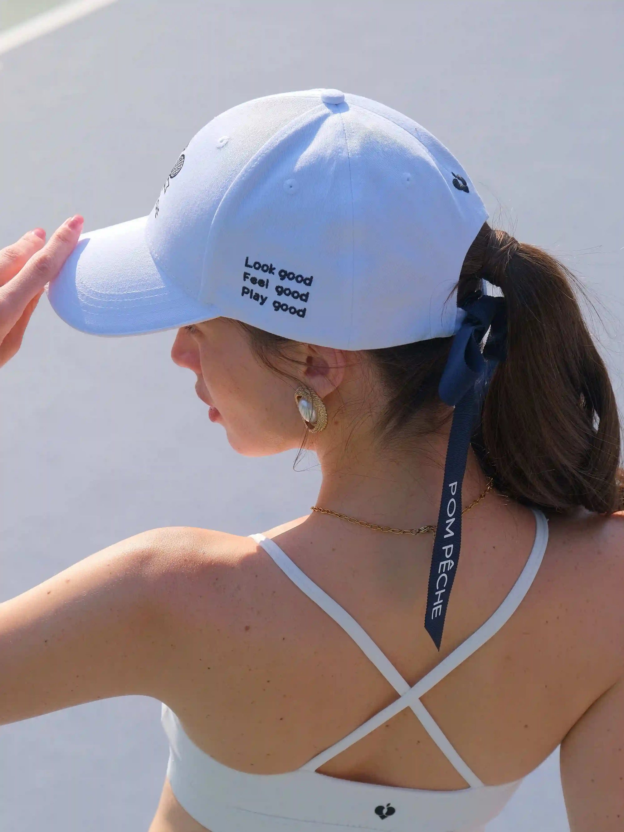 Woman wearing a white cap with text and a white sports bra with thin straps.