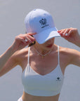 Person wearing a white sports bra and cap with a logo against a light background
