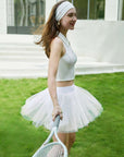 Model wearing a white tulle puff tennis skirt outdoors, showing airy layered mesh and a high-waisted athletic tennis skirt silhouette.