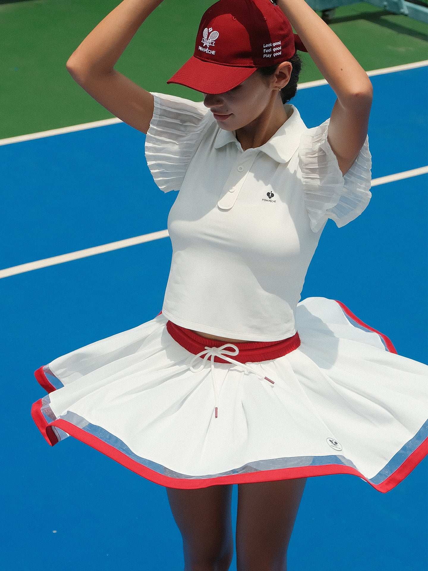 Model wearing a white wavy hem tennis skirt with red trim, showing flowing movement and a high-waisted athletic tennis skirt silhouette on court.