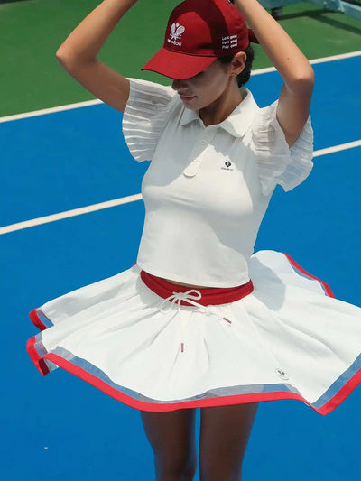 Model wearing a white wavy hem tennis skirt with red trim, showing flowing movement and a high-waisted athletic tennis skirt silhouette on court.