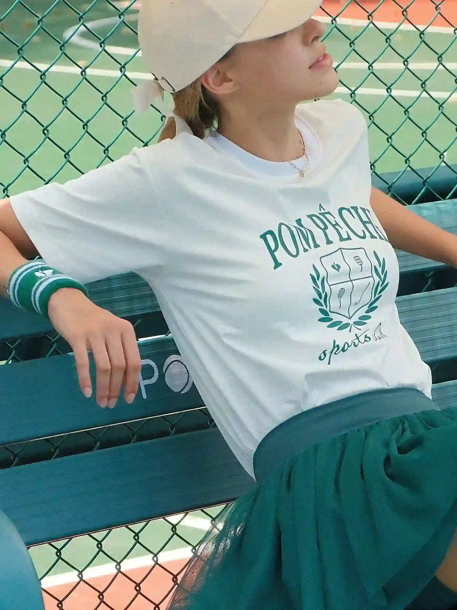 Person wearing a white t-shirt with 'Pompeii' logo on a tennis court