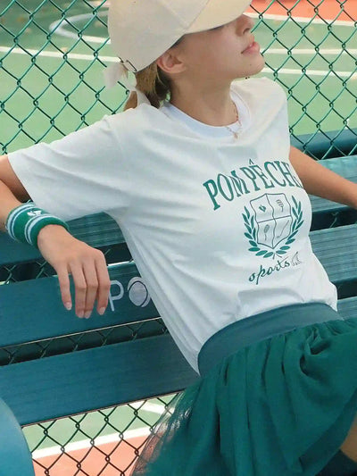 Person wearing a white t-shirt with 'Pompeii' logo on a tennis court