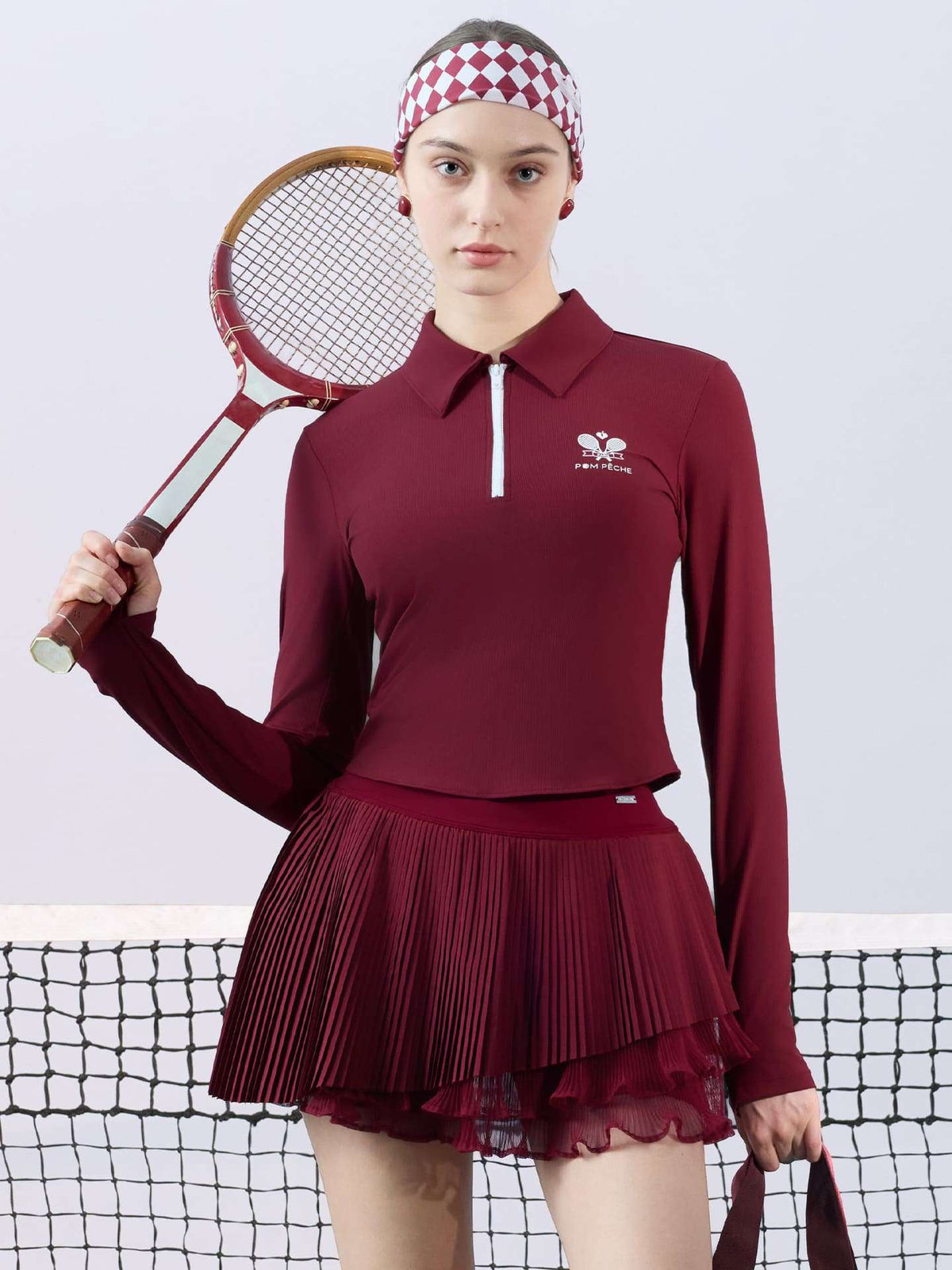 Burgundy pleated tennis skirt paired with long-sleeve top in a court setting