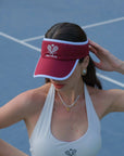 Woman wearing a red visor and white tennis outfit on a tennis court