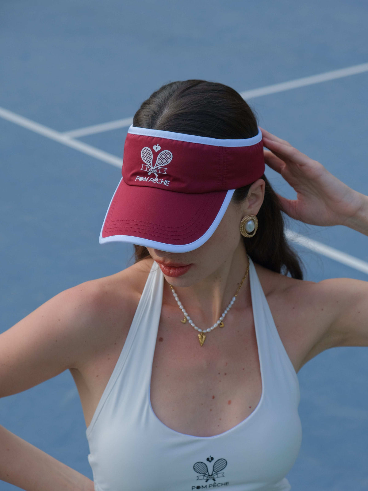 Red tennis visor with embroidered Pom Pêche logo, white trim, worn on the court.